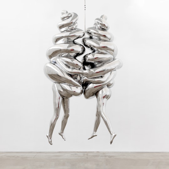 Two suspended and joined silver figures, each with buttocks, legs and arms emerging from a spiral form