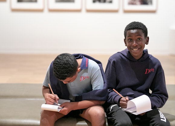 Two students sit on a bench with pencil and paper