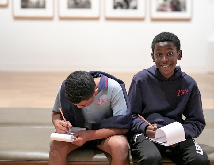 Two students sit on a bench with pencil and paper