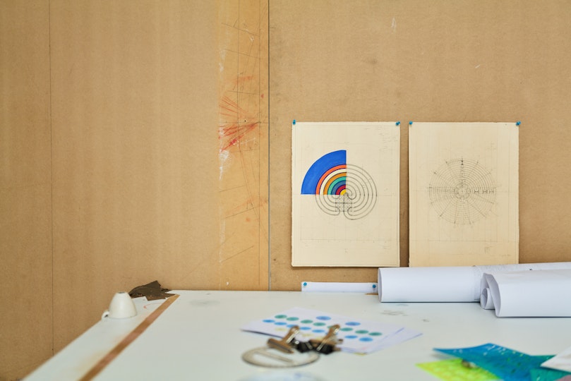 Two illustrations hang on a wall above a table holding rolls of paper and other art materials