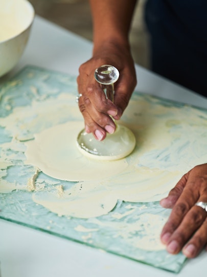 A hand holds a curved glass object on top of cream-coloured substance on a piece of glass