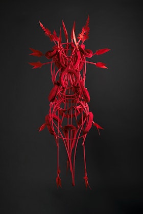 A body-sized sculpture made from bright red cotton webbing, feathers, thread and timber cane.