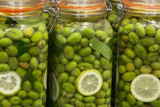 Sealed glass jars full of green olives with a few slices of lemon
