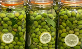 Sealed glass jars full of green olives with a few slices of lemon