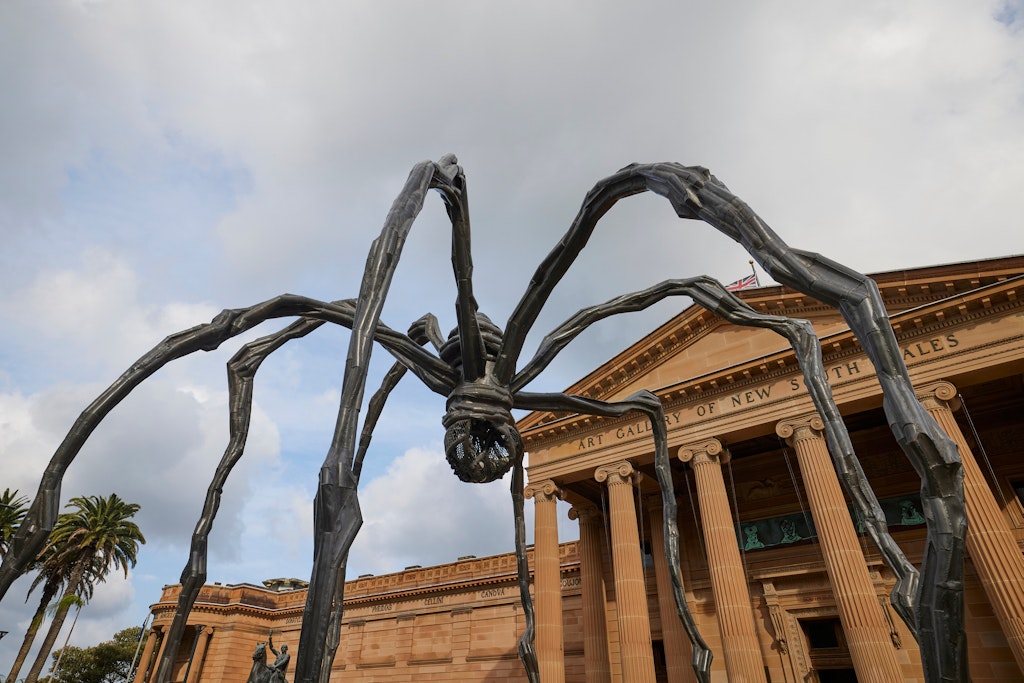 A giant spider sculpture in front of a grand sandstone building with Art Gallery of New South Wales above the portico