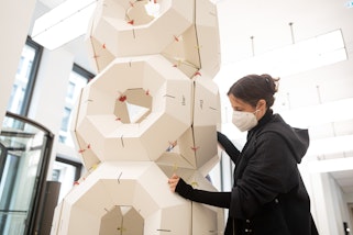 A person wearing a face mask holds a large cardboard geometrical object