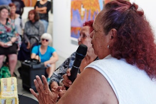 A person holding a microphone in front of a group of people in a gallery space