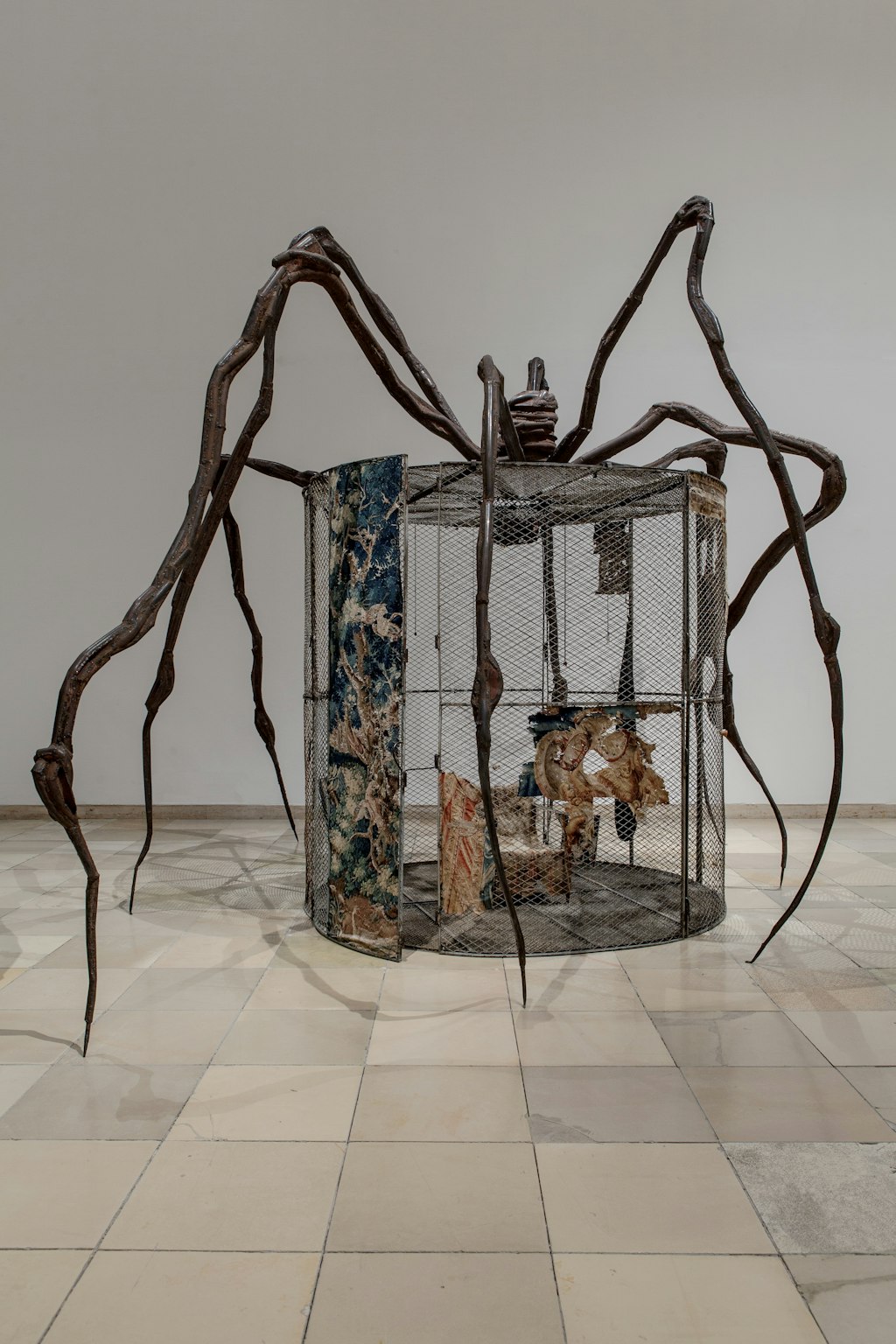 A large bronze sculpture of a spider on top of a tall cage. Inside the cage are textiles and other objects.