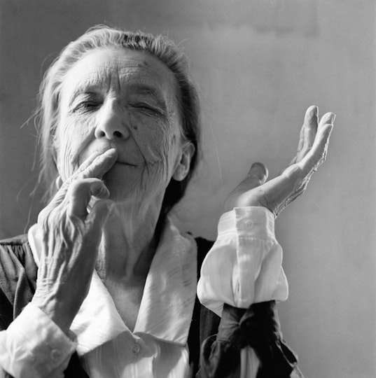 Black and white portrait of Louise Bourgeois wearing a white shirt and black jacket with grey hair pulled back.