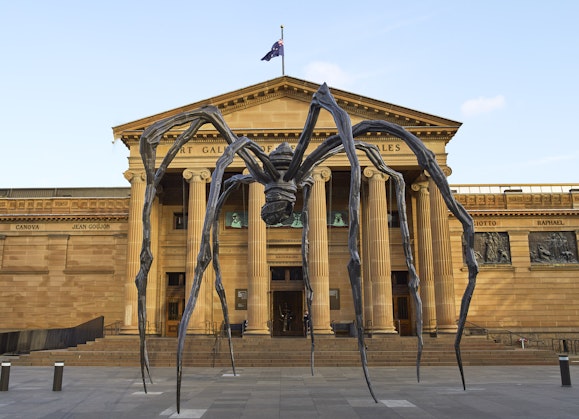 A giant spider sculpture in front of a grand sandstone building with Art Gallery of New South Wales above the portico