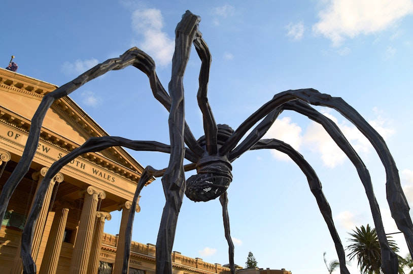A giant spider sculpture in front of a grand sandstone building with Art Gallery of New South Wales above the portico