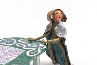 A ceramic figure leans on a ceramic table