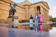 Three people stand at the front of a large sandstone building next to a sculpture of a person on a horse