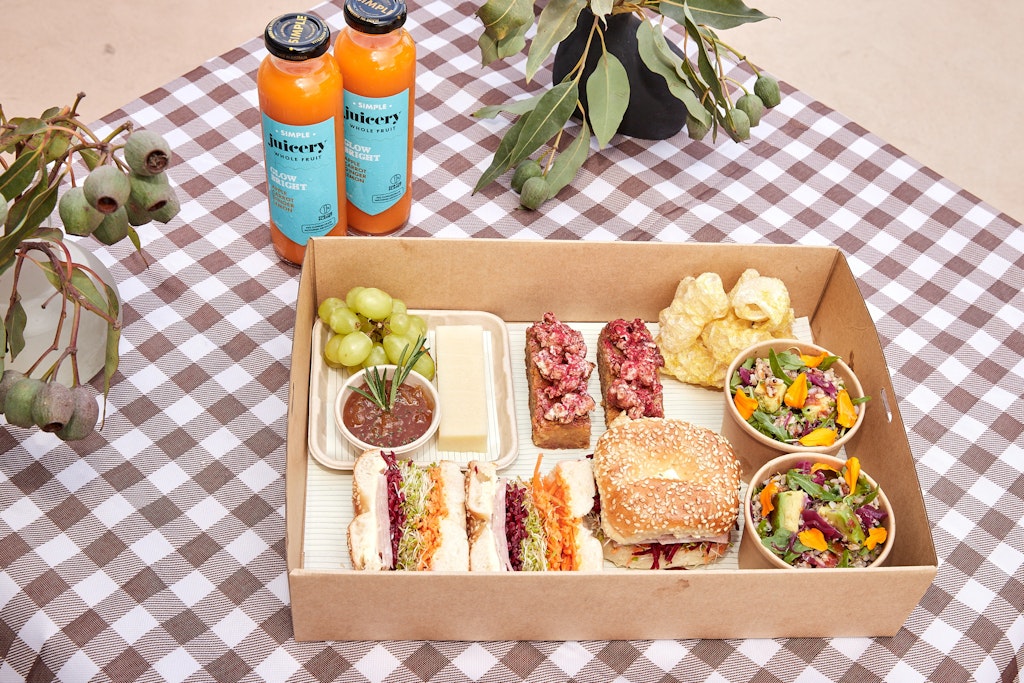 Two bottles of drink and a large open box holding a variety of food, including sandwiches and salads