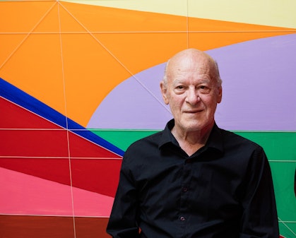 A person in a black shirt against a background of different shapes in bright solid colours