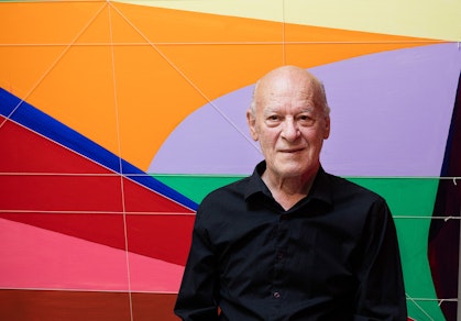 A person in a black shirt against a background of different shapes in bright solid colours