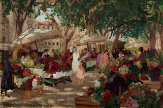 People in an outdoor market of flower stalls under trees and umbrellas with buildings in the background