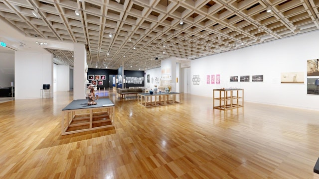 A large gallery space with works on the wall and on wooden plinths.