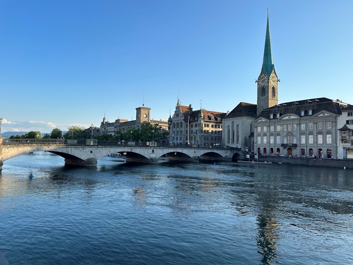 A low bridge across water leads to historic city buildings, including a church with a tall spire