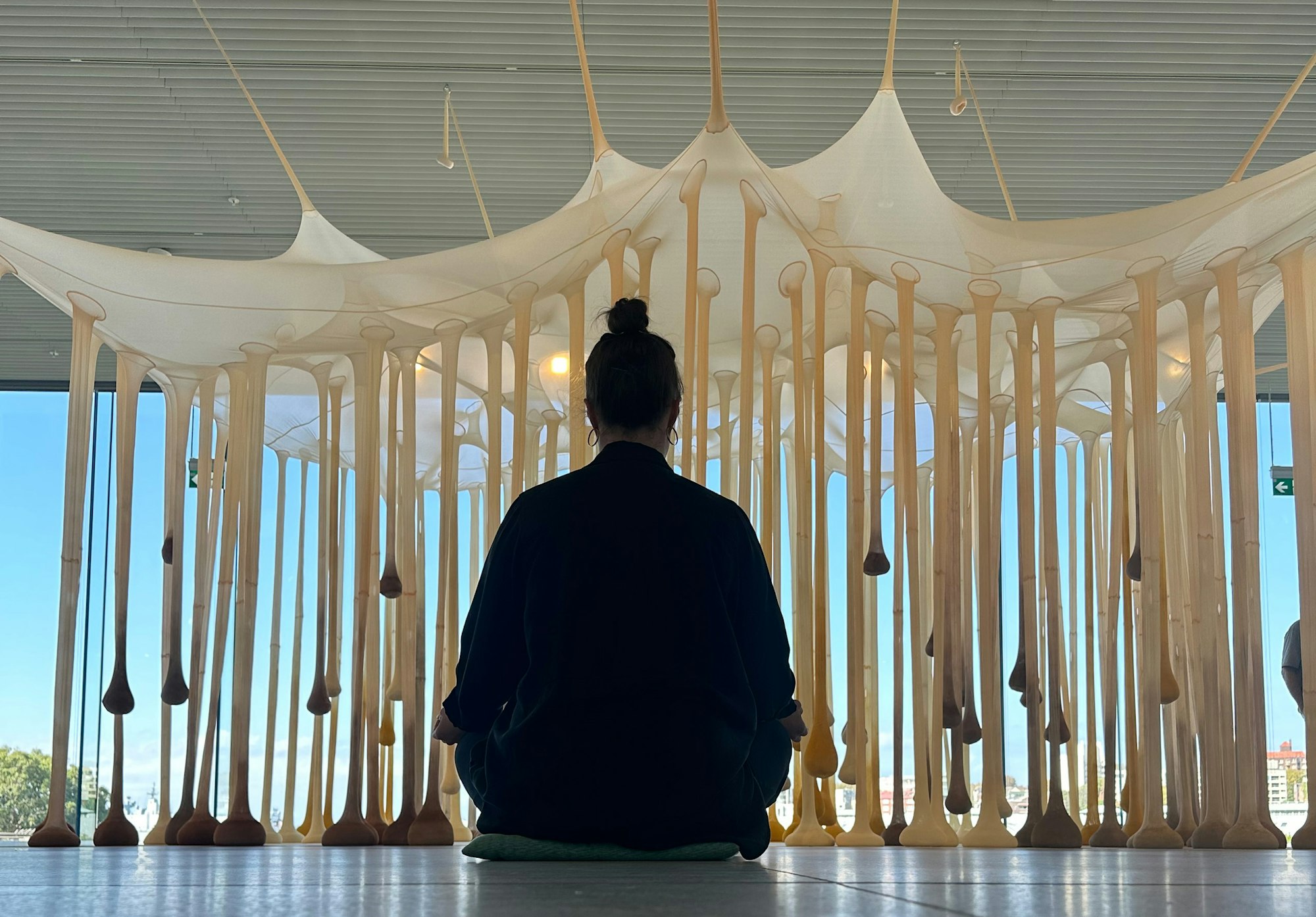 A person seated on a cushion on the floor in front of a large hanging installation