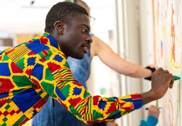 A person in a colourful shirt draws on a wall next to other people