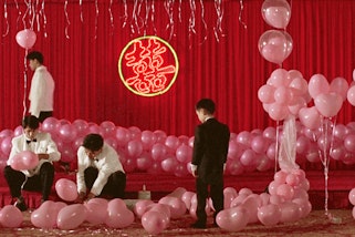 A child and three adults among pink balloons in front of a red curtain with a neon sign