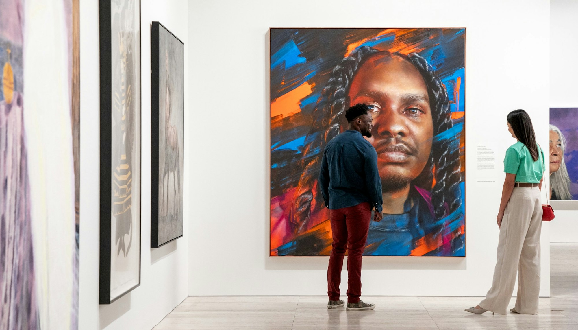 Two people in front of a large painting of a person's head and shoulders