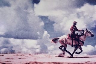 A cowboy galloping on a horse on a sandy plain with clouded sky in the background