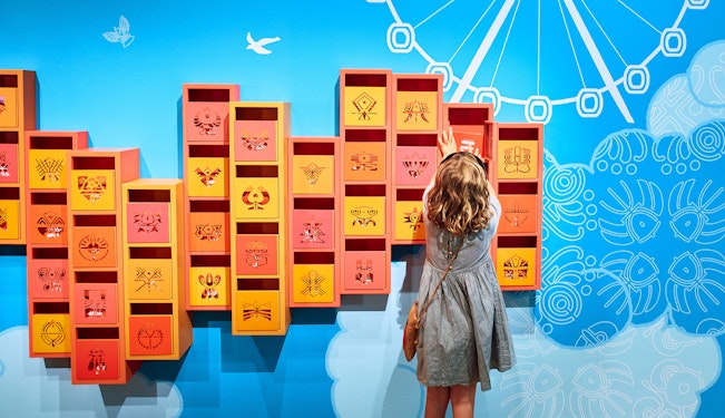Child opens a colourful box mounted on a blue wall