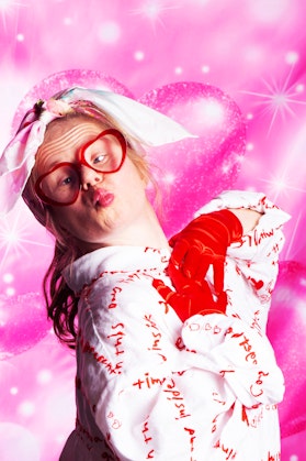A woman with glasses pouting in front of a pink background
