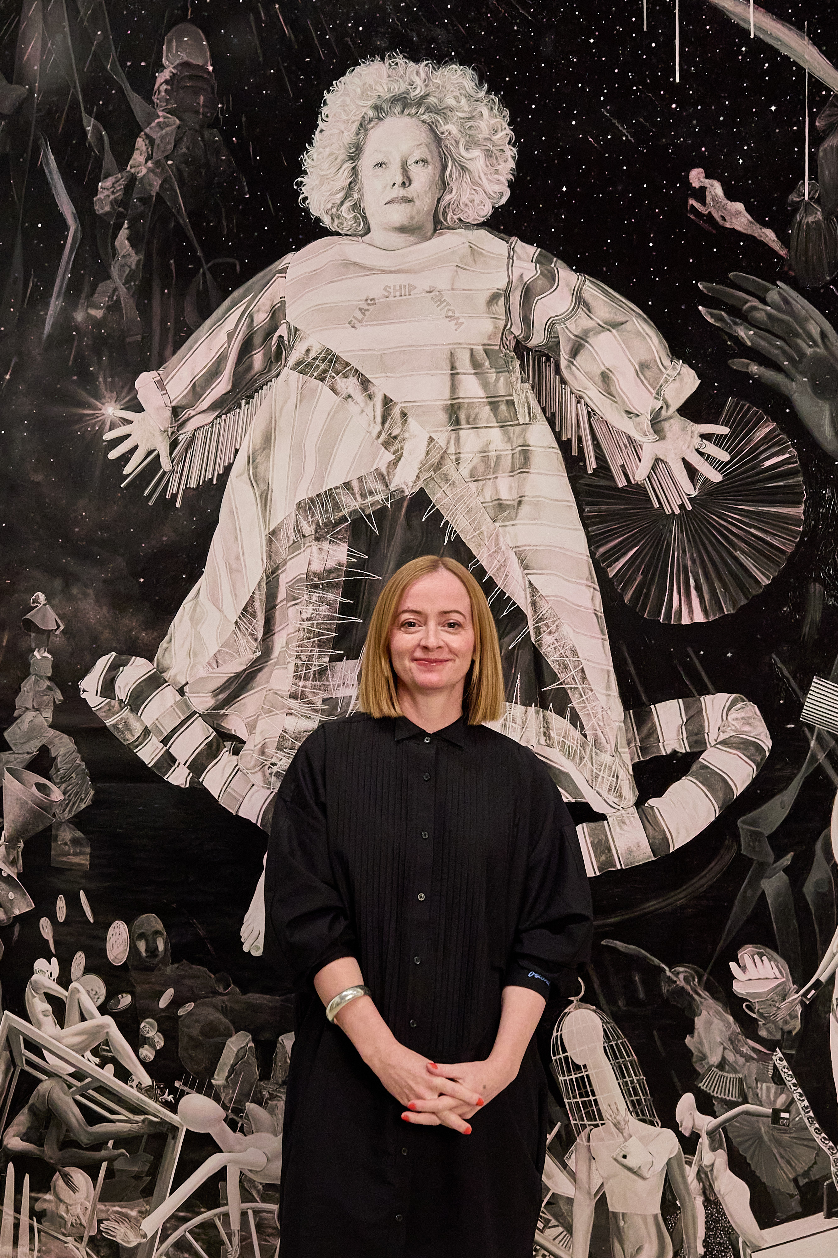 A lady wearing a black dress stands in front a large portrait painting