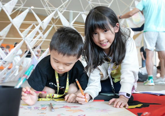 Two children sit on the floor of an art gallery, colouring together with focus and creativity