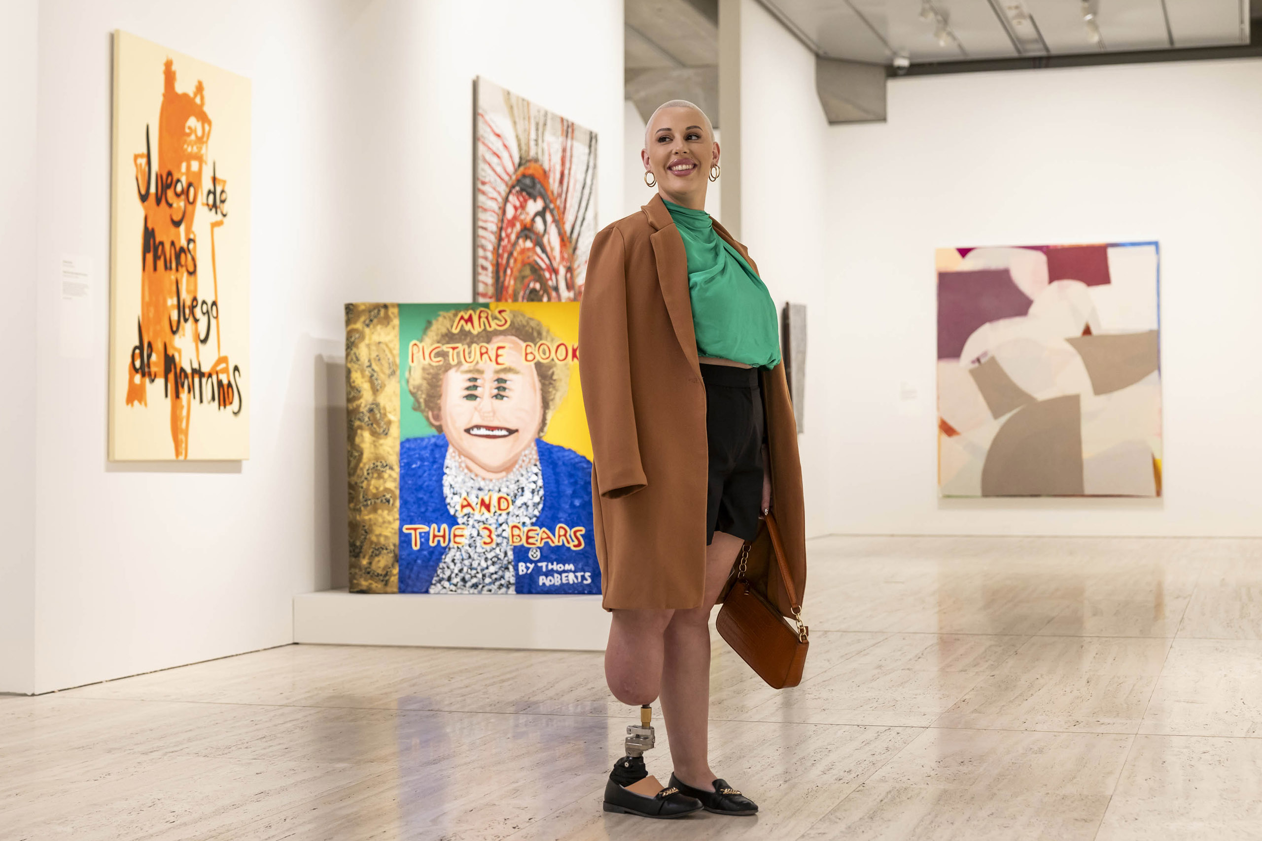 Visitor smiling with large, colourful paintings displayed on the wall behind them