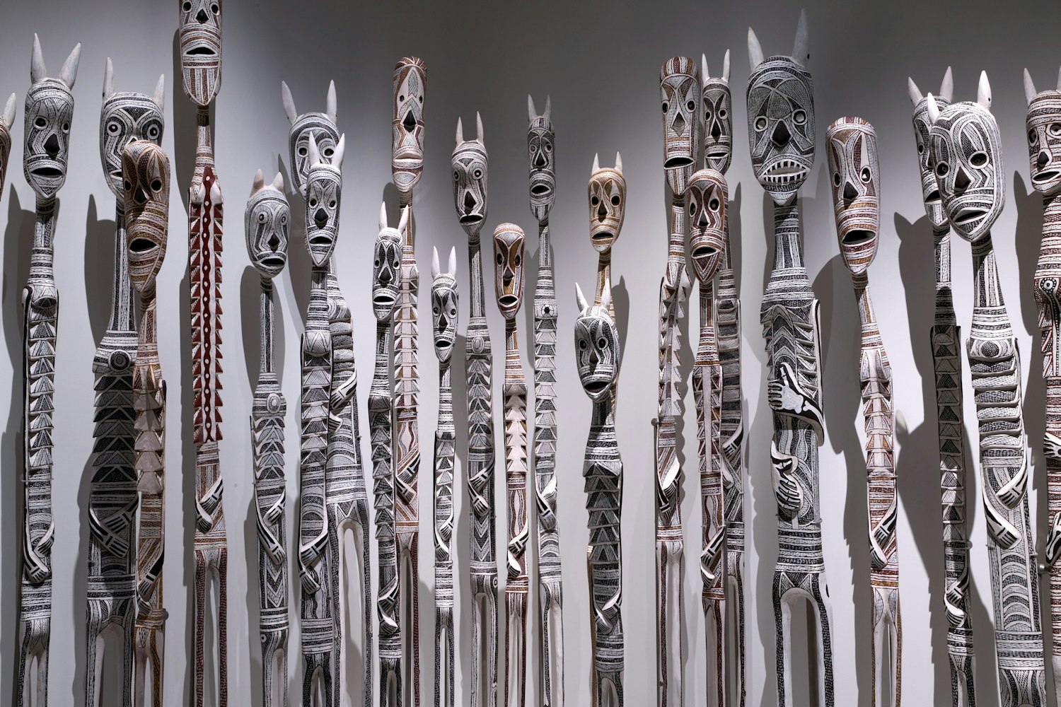 Group of tall, thin, creature-like sculptures with painted faces and bodies.