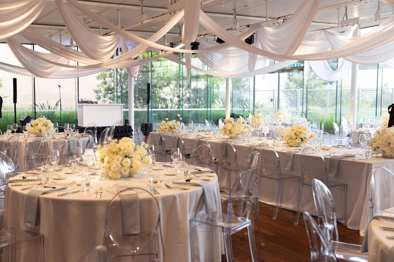 Various tables are cloaked with white fabric and a white floral arrangement in the centre