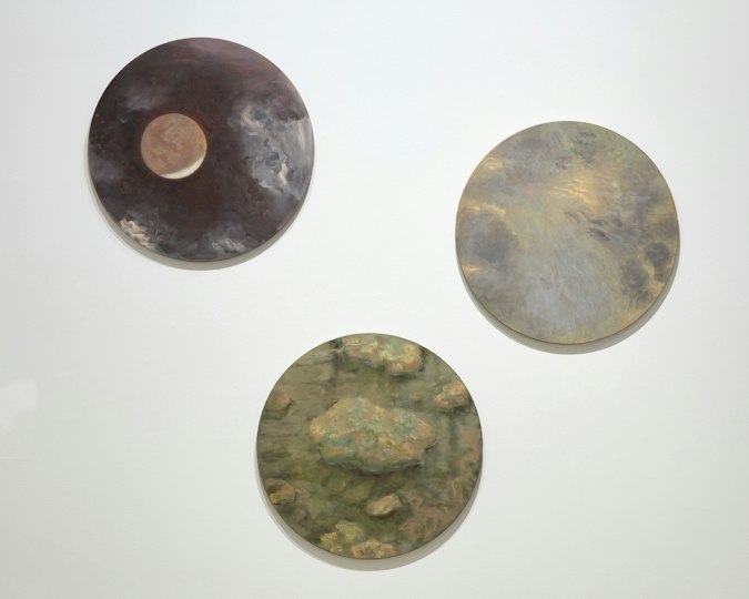 Three circular paintings on a white wall,  depicting atmospheric scenes in earthy and muted tones