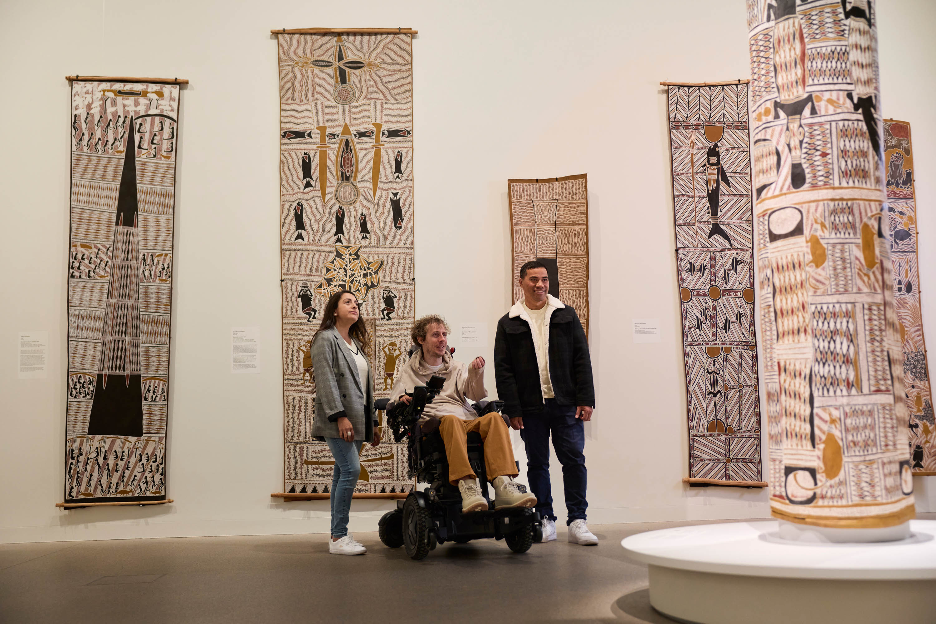 Person viewing bark paintings and a sculpture in an art gallery