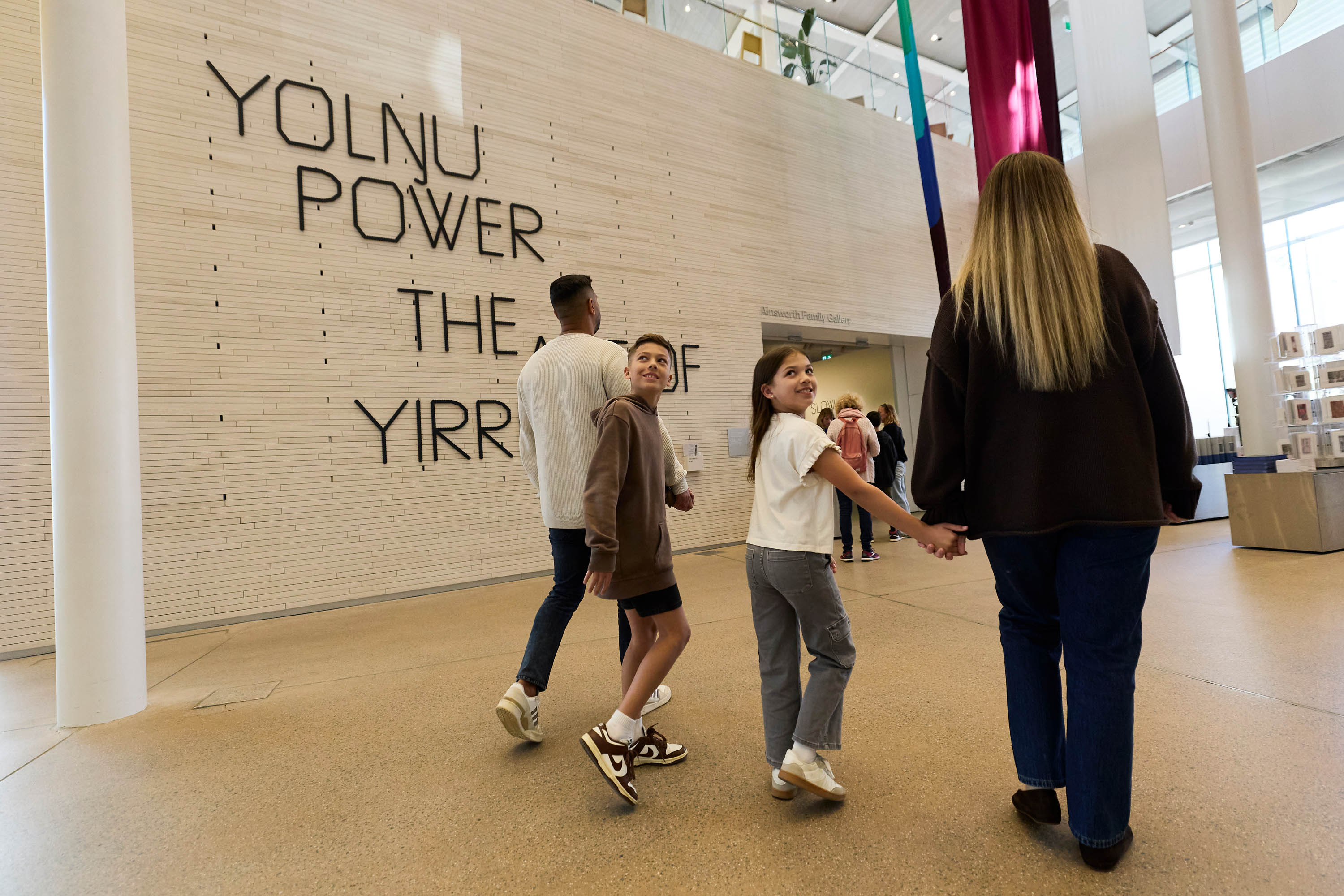 Family of two adults and two children walking through a light-filled art gallery