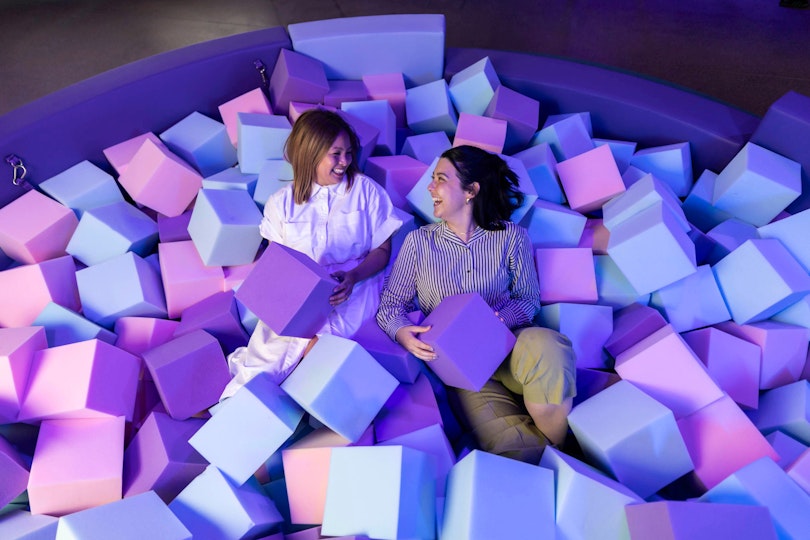 Visitors playing in a pit of purple and pink foam cubes