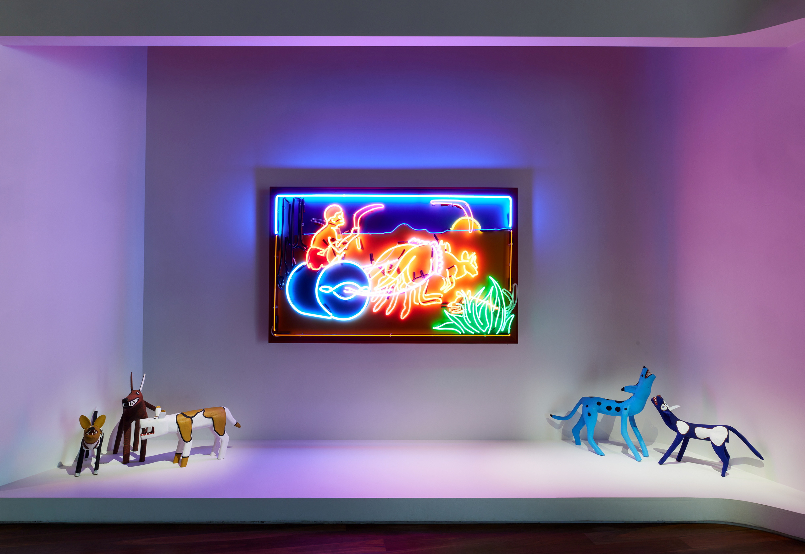 Neon artwork displayed on a gallery wall, flanked by brightly coloured dog sculptures.