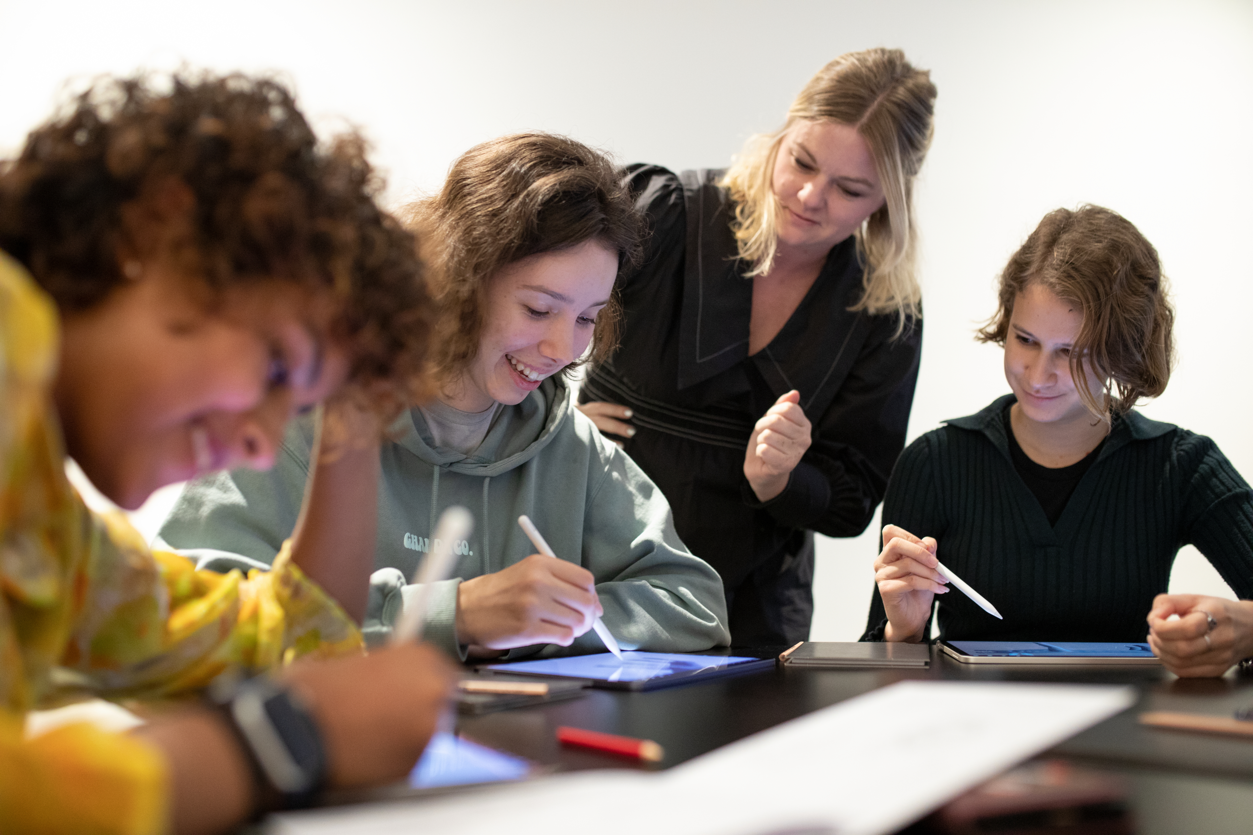 Three senior secondary students sitting at a table with a teacher standing by them