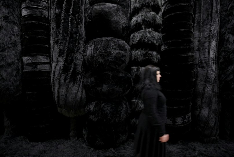 Woman in black clothing walks past a large abstract black fur sculpture