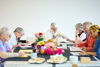 Elderly people painting together at a table decorated with flowers