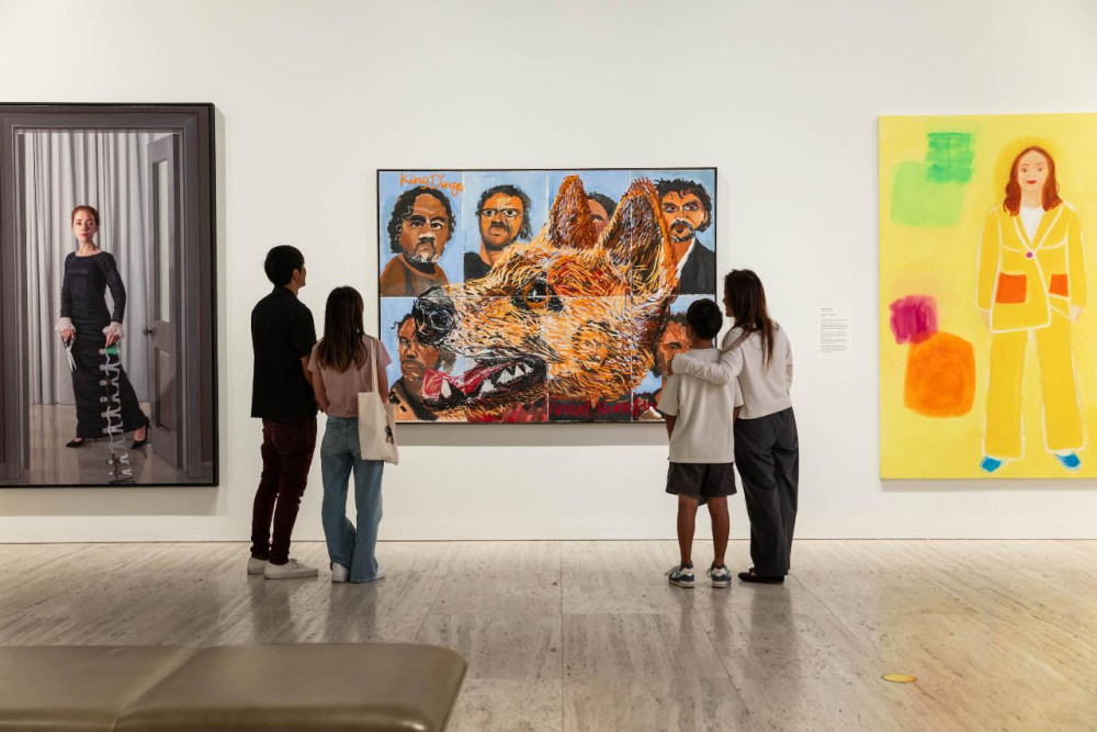Visitors stand in an art exhibition, viewing large paintings on display