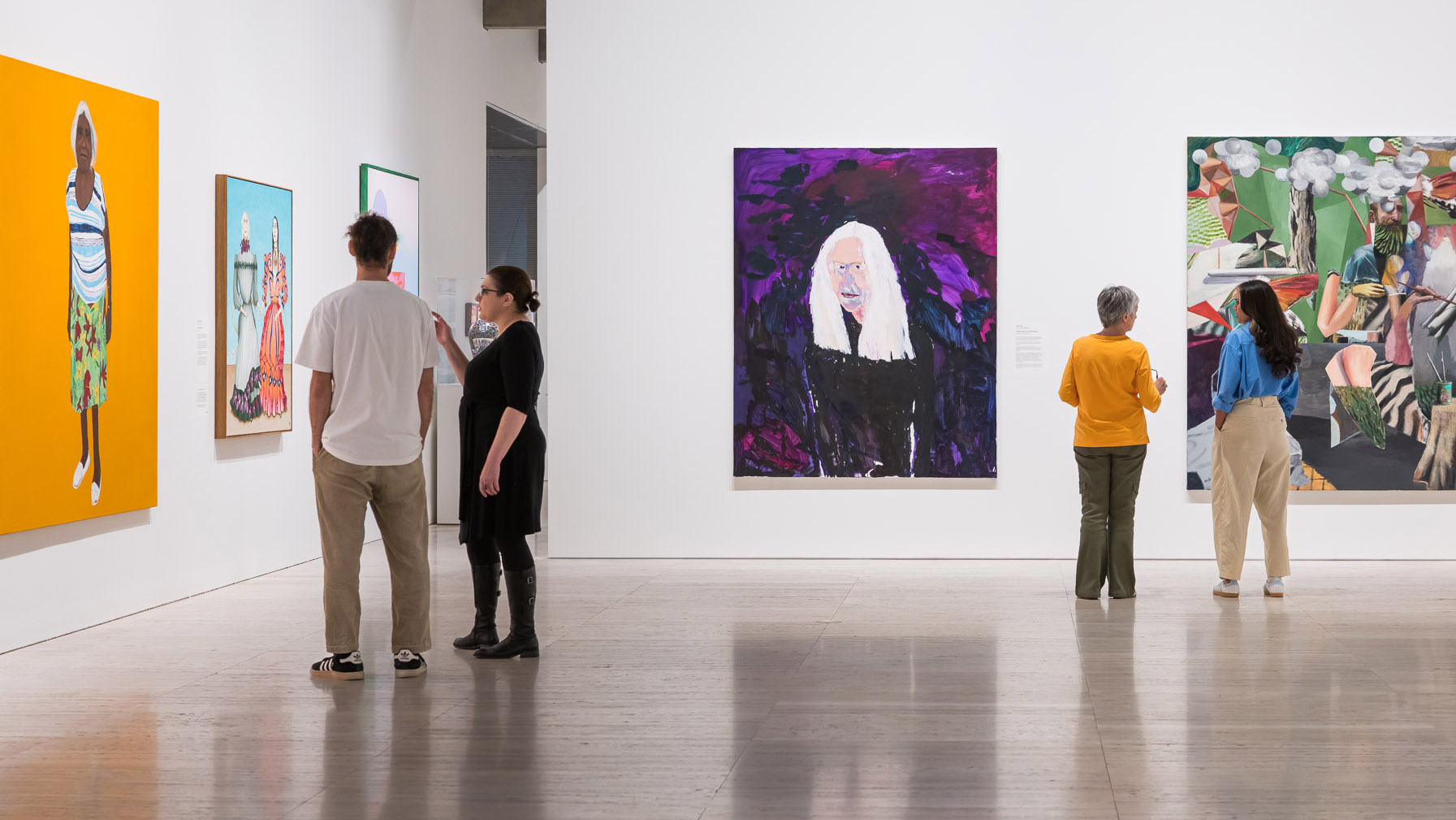 Visitors stand in an art exhibition, viewing large paintings on display