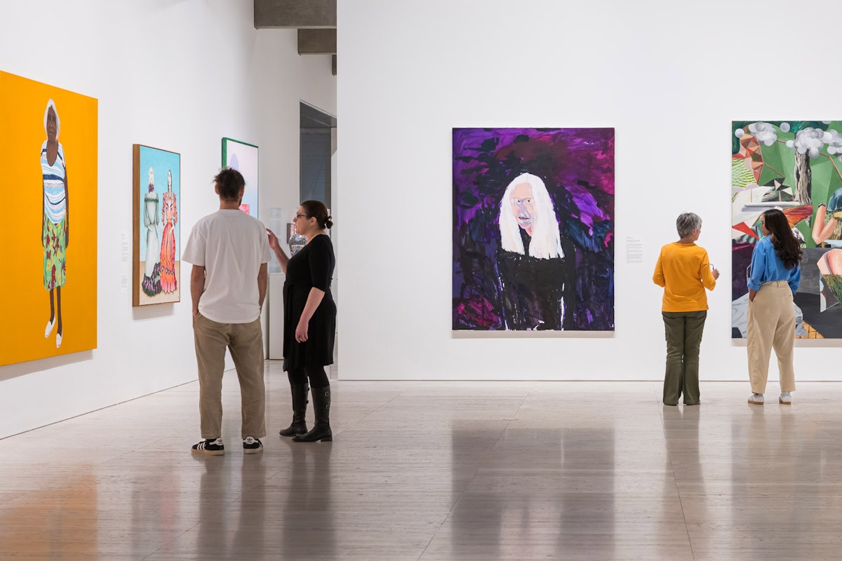 Visitors stand in an art exhibition, viewing large paintings on display