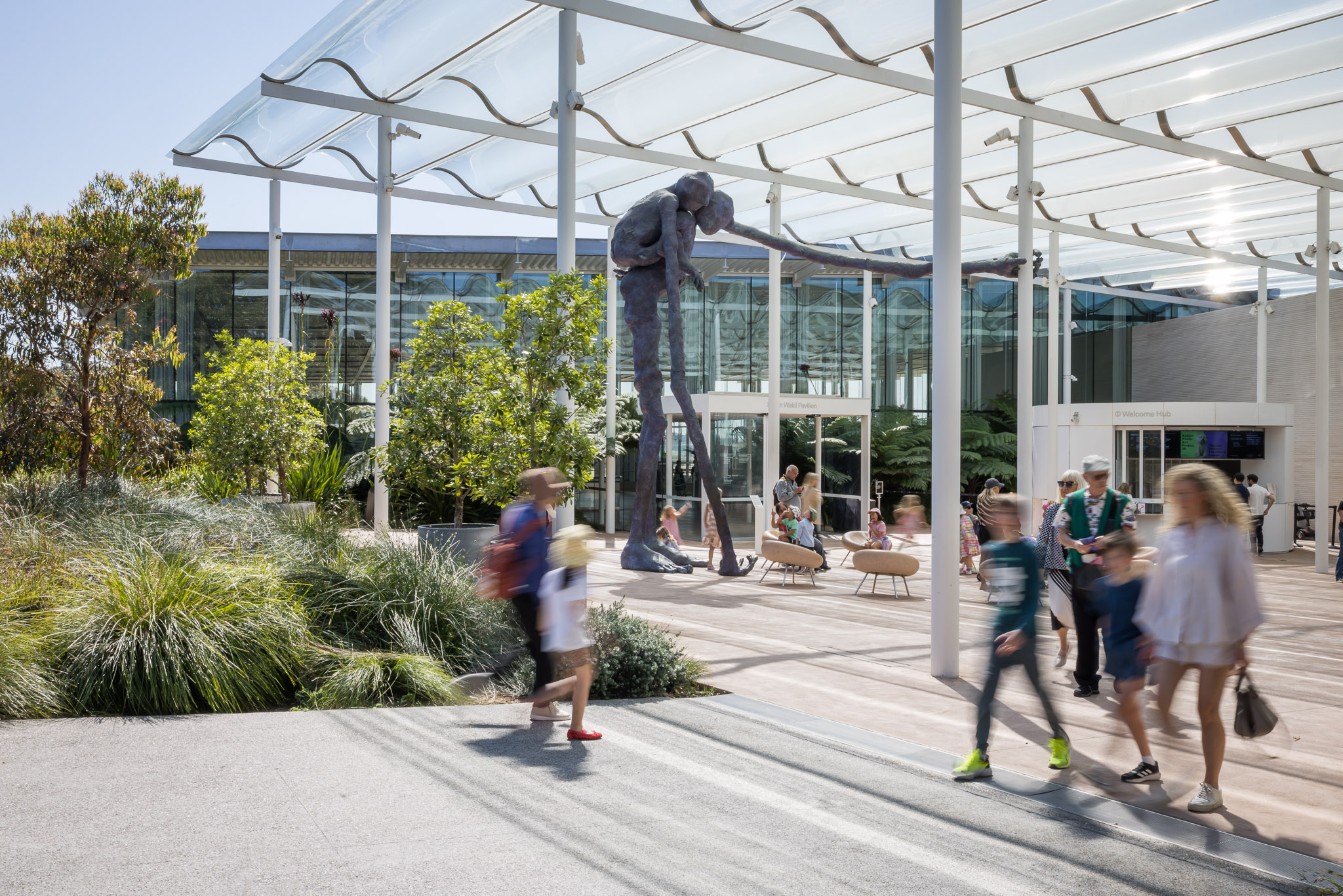 People walking towards a glass-walled building with a large figurative sculpture