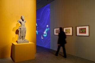 A gallery space featuring a sculpture, a digital projection and framed paintings.