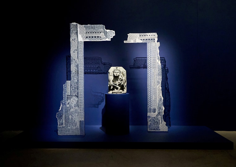 A sculpture with a fabric art installation around it, displayed against a dark blue wall.