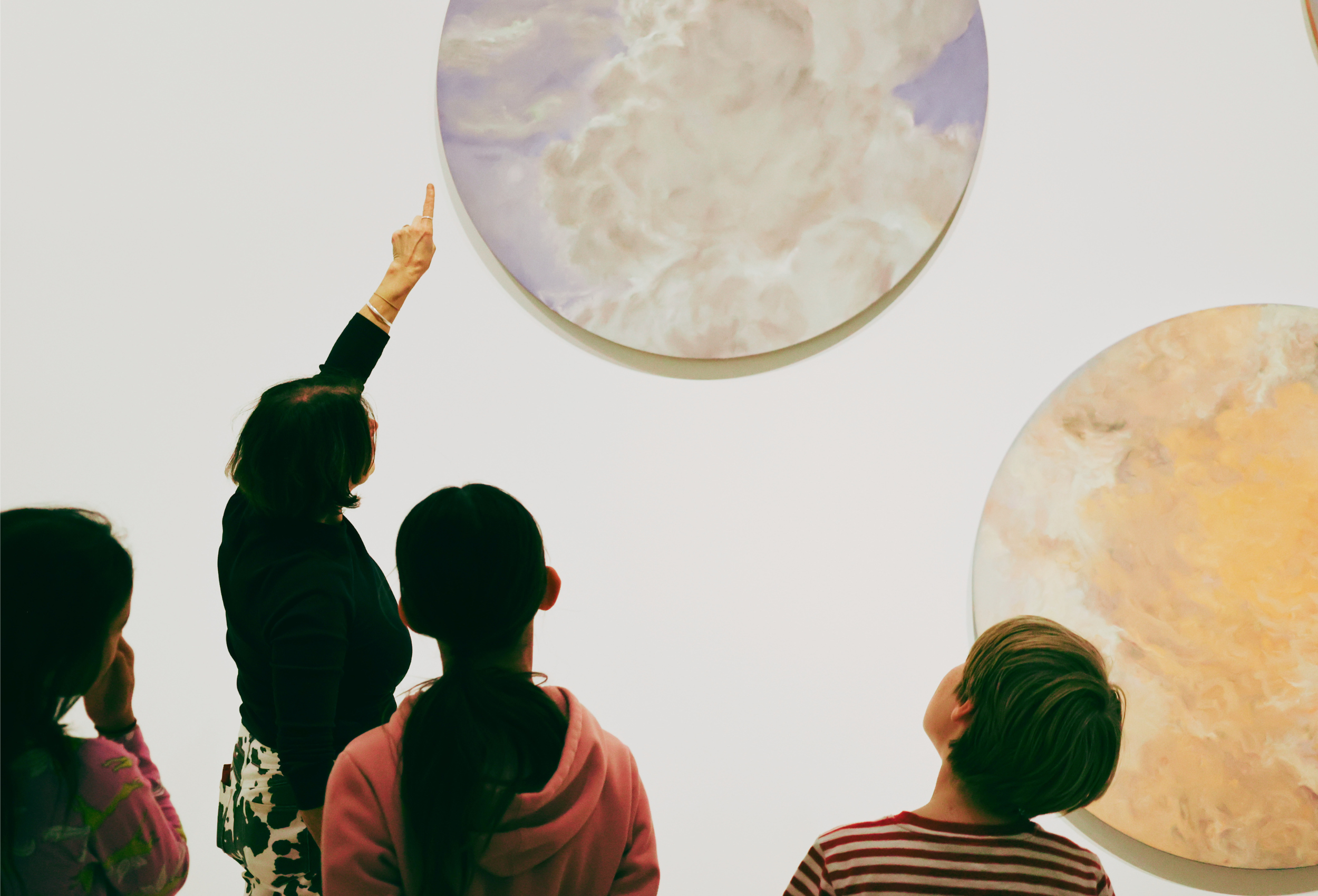 A woman pointing to a artwork to some children